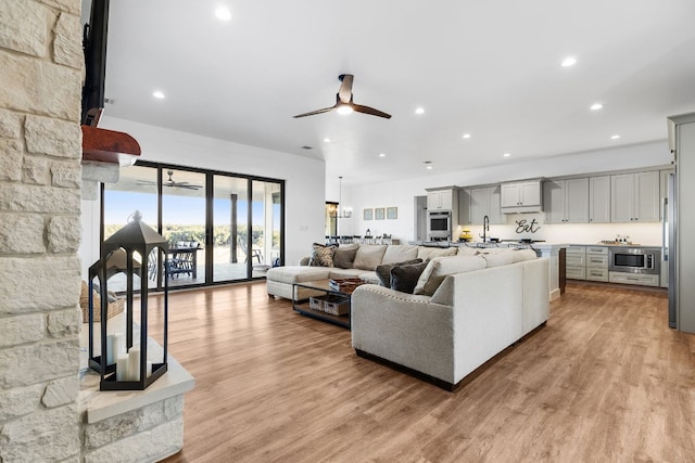 living room with light wood-type flooring, ceiling fan, and sink