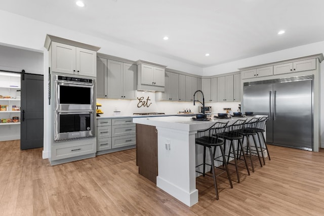 kitchen with stainless steel appliances, a kitchen island with sink, light hardwood / wood-style flooring, and a barn door