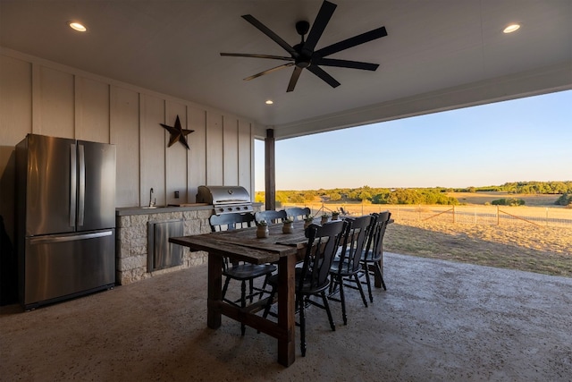 patio terrace at dusk with an outdoor kitchen, area for grilling, ceiling fan, sink, and a rural view