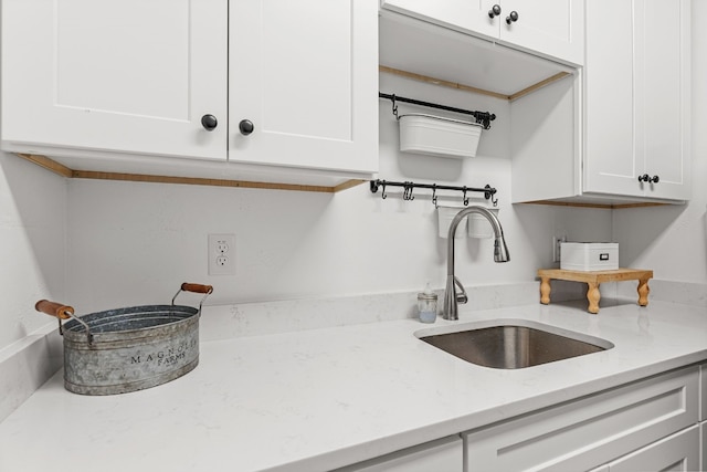 kitchen with white cabinetry, sink, and light stone counters