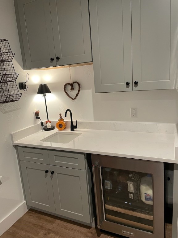 bar featuring gray cabinets, sink, beverage cooler, and wood-type flooring