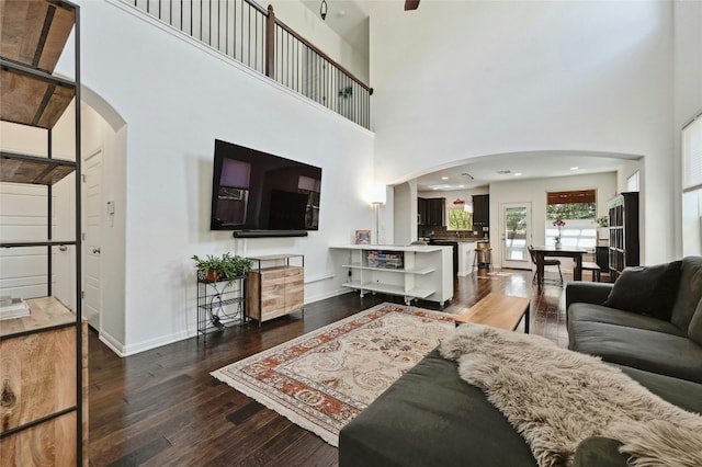 living room with arched walkways, a towering ceiling, baseboards, and wood finished floors