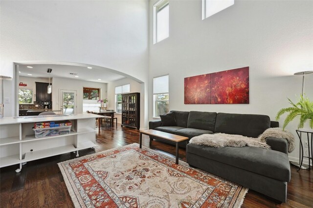 living room featuring arched walkways, dark wood-type flooring, and a healthy amount of sunlight