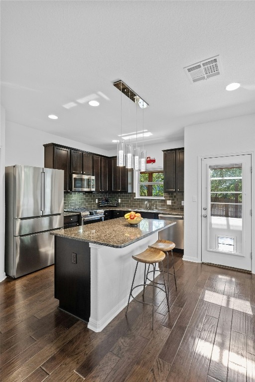 kitchen featuring stainless steel appliances, visible vents, dark brown cabinets, a center island, and dark wood-style floors