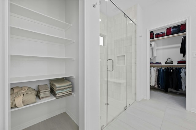 full bathroom with a spacious closet, a stall shower, and baseboards