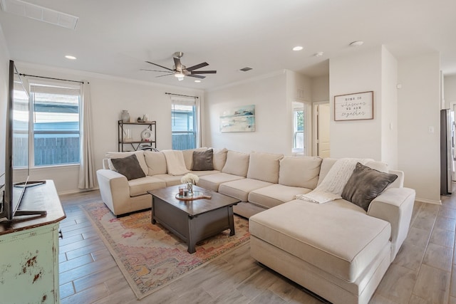 living room with ornamental molding, a wealth of natural light, ceiling fan, and light wood-type flooring