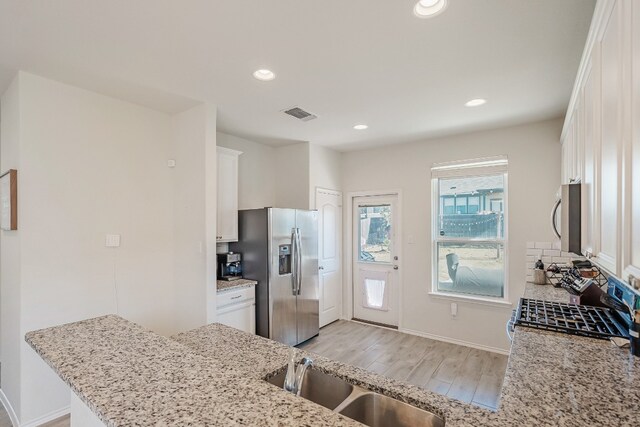 kitchen with light stone countertops, white cabinetry, stainless steel appliances, and light hardwood / wood-style floors