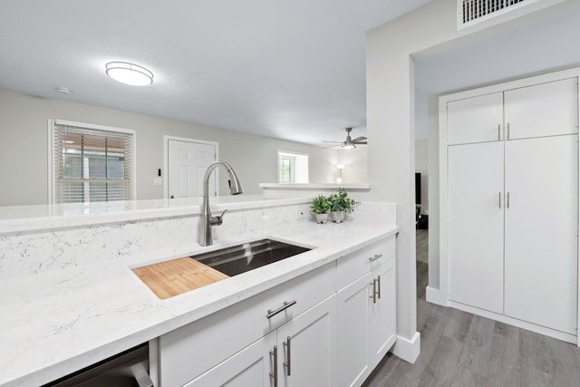 kitchen featuring light stone countertops, white cabinetry, light hardwood / wood-style flooring, and sink