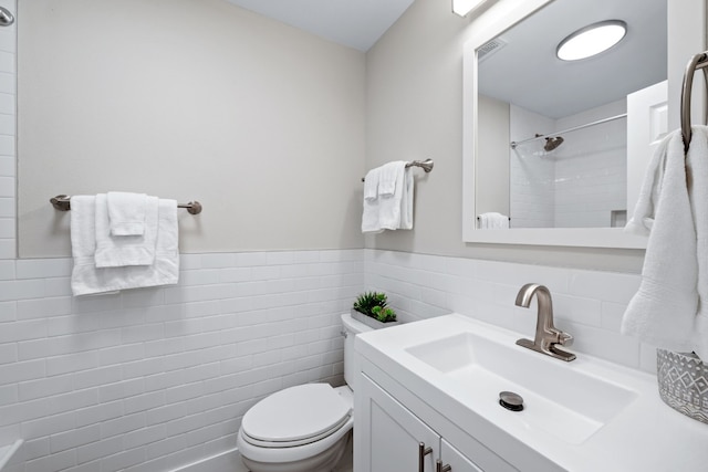 bathroom with tiled shower, vanity, toilet, and tile walls