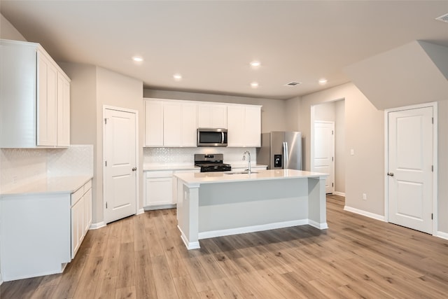 kitchen featuring white cabinets, stainless steel appliances, decorative backsplash, sink, and a center island with sink