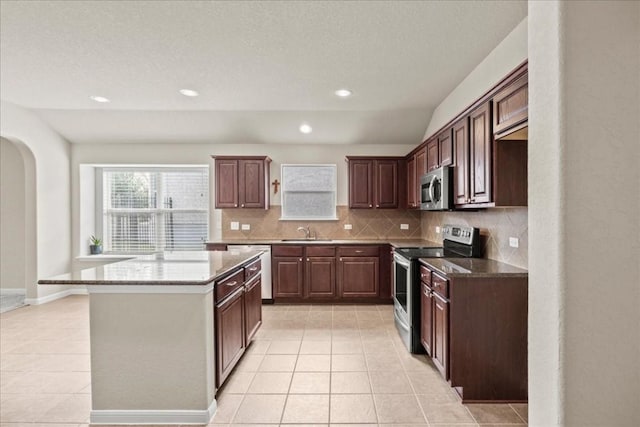 kitchen with light stone counters, stainless steel appliances, sink, light tile patterned floors, and a kitchen island