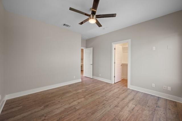 unfurnished bedroom with a closet, ceiling fan, hardwood / wood-style flooring, and a walk in closet