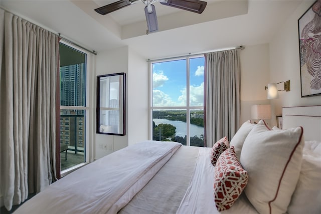 bedroom featuring a water view, ceiling fan, access to exterior, and a tray ceiling