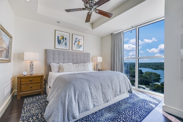 bedroom with a tray ceiling, ceiling fan, a water view, and dark hardwood / wood-style floors