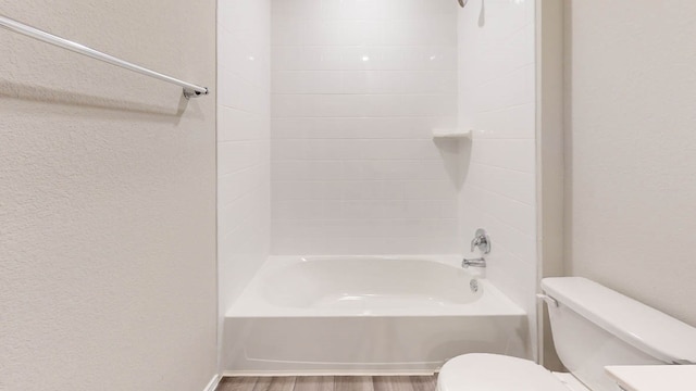 bathroom with tiled shower / bath combo, hardwood / wood-style flooring, and toilet