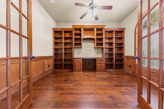 unfurnished office featuring ceiling fan, french doors, dark hardwood / wood-style flooring, wood walls, and built in desk