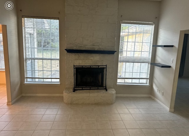 unfurnished living room with light tile patterned floors, a stone fireplace, and a wealth of natural light