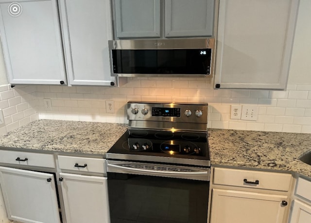 kitchen featuring backsplash, light stone countertops, white cabinets, and stainless steel appliances