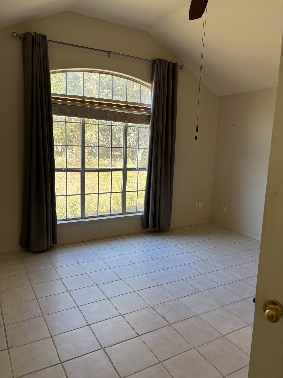 empty room featuring ceiling fan, plenty of natural light, light tile patterned floors, and lofted ceiling