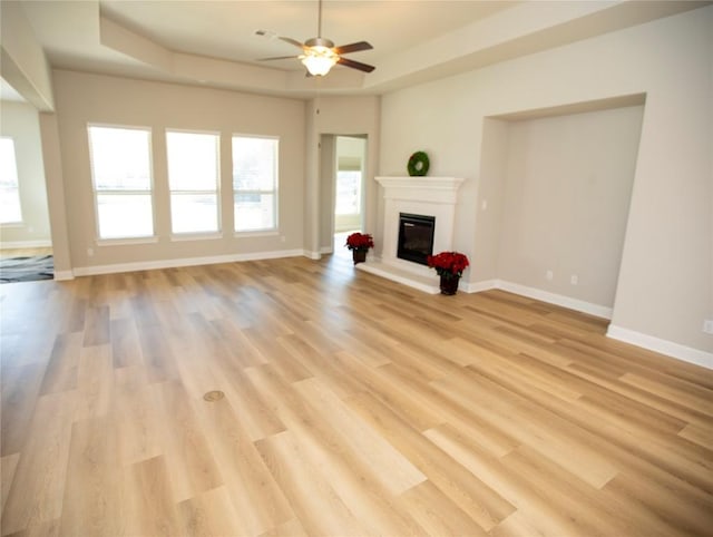 unfurnished living room with a raised ceiling, light hardwood / wood-style flooring, and ceiling fan