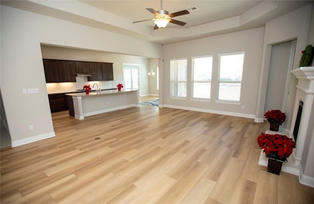 living room with a raised ceiling, ceiling fan, sink, and light wood-type flooring