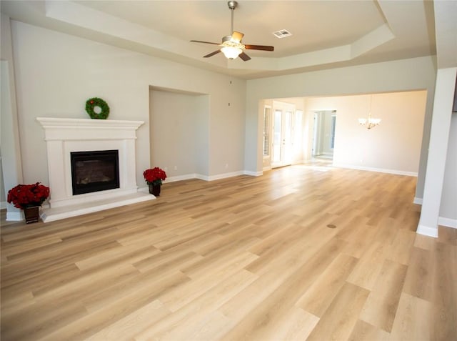 unfurnished living room with a raised ceiling, light hardwood / wood-style floors, and ceiling fan with notable chandelier