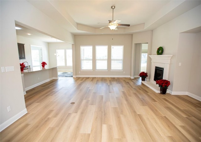 unfurnished living room featuring ceiling fan, light hardwood / wood-style floors, and a raised ceiling