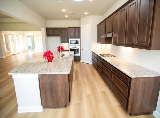 kitchen with light stone countertops, a center island, stainless steel appliances, and light hardwood / wood-style floors