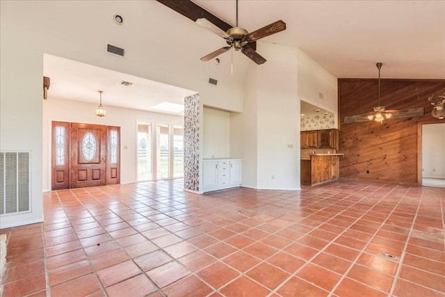 unfurnished living room featuring tile patterned flooring, ceiling fan, wood walls, and high vaulted ceiling