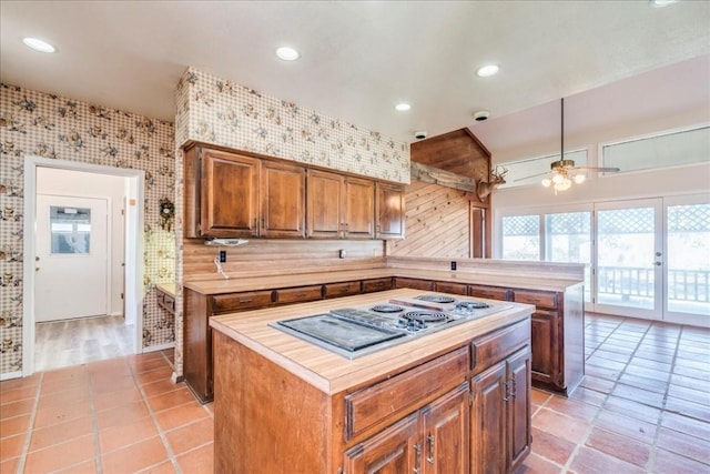 kitchen featuring ceiling fan, tasteful backsplash, kitchen peninsula, stainless steel gas stovetop, and a kitchen island