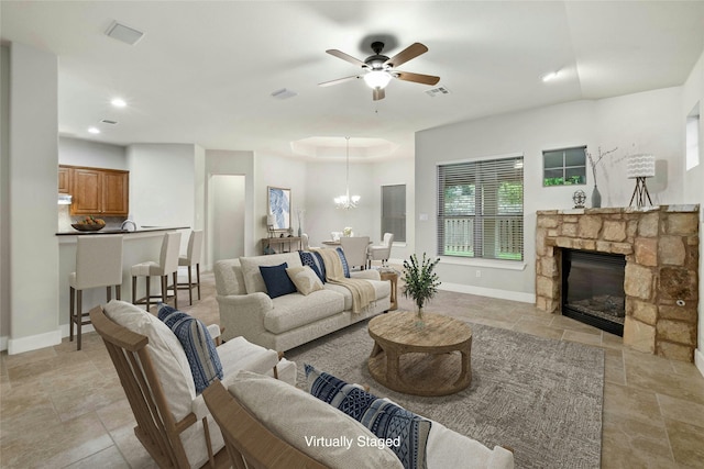 living room featuring ceiling fan with notable chandelier, a raised ceiling, and a fireplace