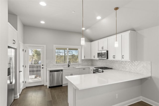 kitchen featuring kitchen peninsula, vaulted ceiling, decorative light fixtures, white cabinets, and appliances with stainless steel finishes