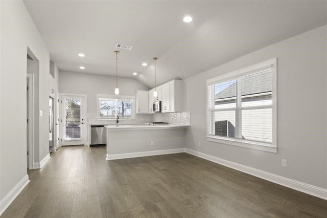 kitchen with pendant lighting, kitchen peninsula, vaulted ceiling, appliances with stainless steel finishes, and white cabinetry