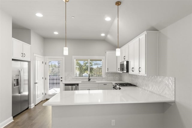 kitchen featuring lofted ceiling, kitchen peninsula, appliances with stainless steel finishes, decorative light fixtures, and white cabinetry