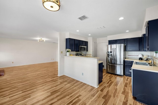 kitchen with appliances with stainless steel finishes, blue cabinets, sink, decorative backsplash, and light hardwood / wood-style flooring