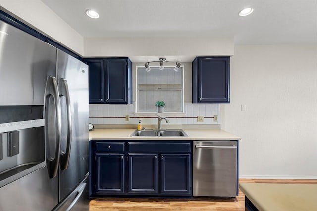 kitchen with sink, light hardwood / wood-style flooring, appliances with stainless steel finishes, blue cabinets, and decorative backsplash