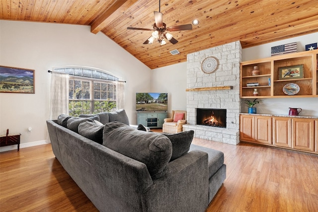 living room featuring beam ceiling, light wood-type flooring, a stone fireplace, and ceiling fan