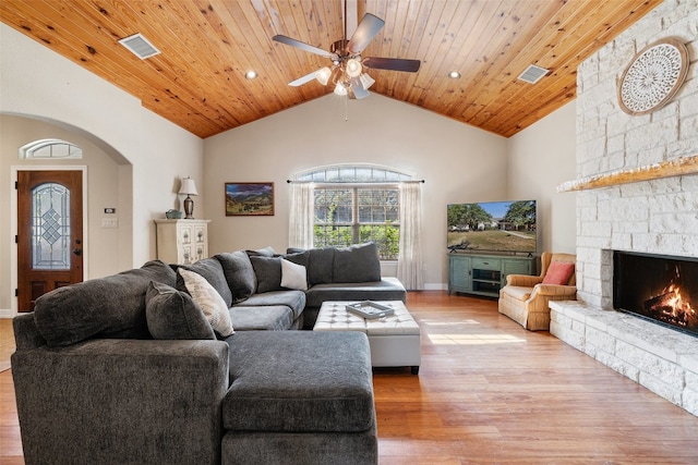 living room featuring ceiling fan, a stone fireplace, wood ceiling, and light hardwood / wood-style flooring