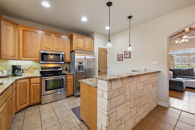 kitchen with light stone countertops, ceiling fan, pendant lighting, and appliances with stainless steel finishes