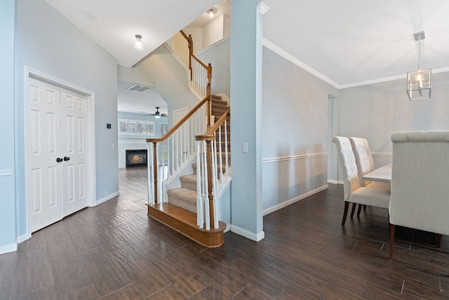 interior space with crown molding, dark wood-type flooring, a tile fireplace, and ceiling fan with notable chandelier