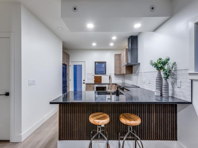 kitchen featuring kitchen peninsula, sink, wall chimney exhaust hood, and a breakfast bar area