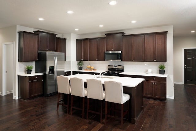 kitchen with tasteful backsplash, dark hardwood / wood-style floors, a kitchen bar, a kitchen island with sink, and appliances with stainless steel finishes