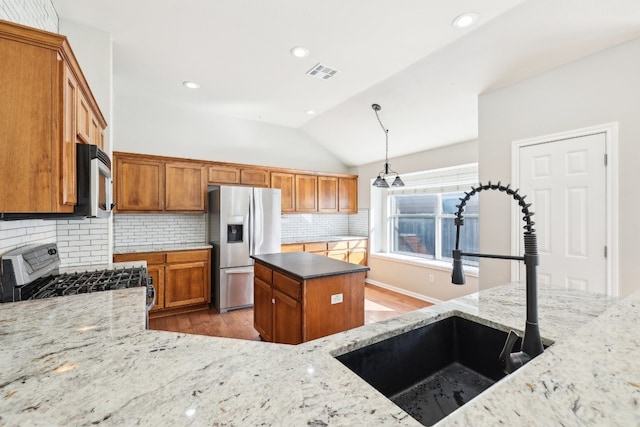 kitchen with light stone countertops, appliances with stainless steel finishes, decorative light fixtures, and vaulted ceiling