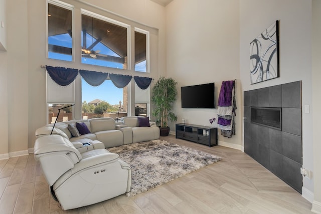 living room with ceiling fan, light wood-type flooring, a towering ceiling, and a tile fireplace