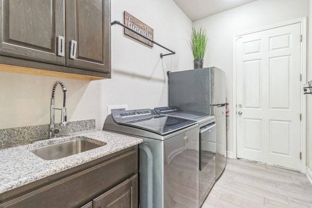 laundry area featuring washer and dryer, light hardwood / wood-style flooring, cabinets, and sink