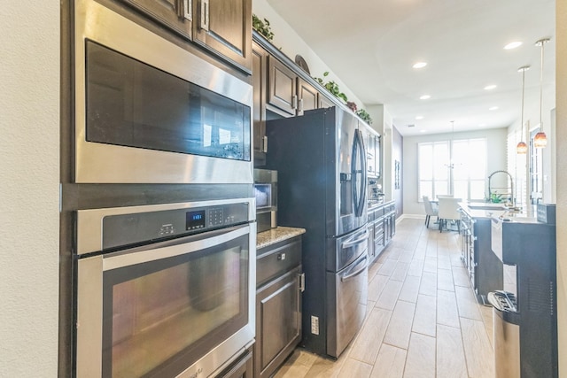 kitchen featuring dark brown cabinetry, hanging light fixtures, stainless steel appliances, and light hardwood / wood-style flooring