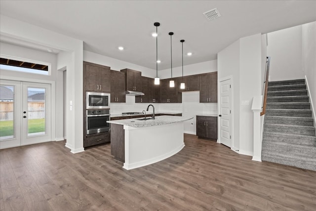 kitchen featuring french doors, stainless steel appliances, dark wood-type flooring, sink, and a center island with sink