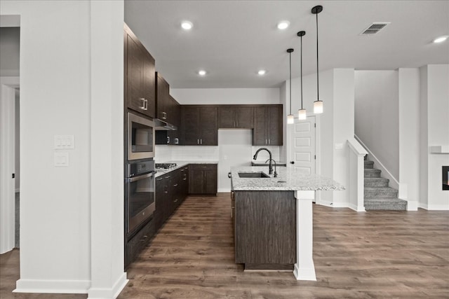 kitchen featuring dark hardwood / wood-style flooring, stainless steel oven, a center island with sink, and sink