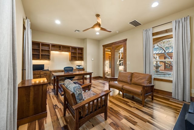 office space with ceiling fan, built in desk, and wood-type flooring