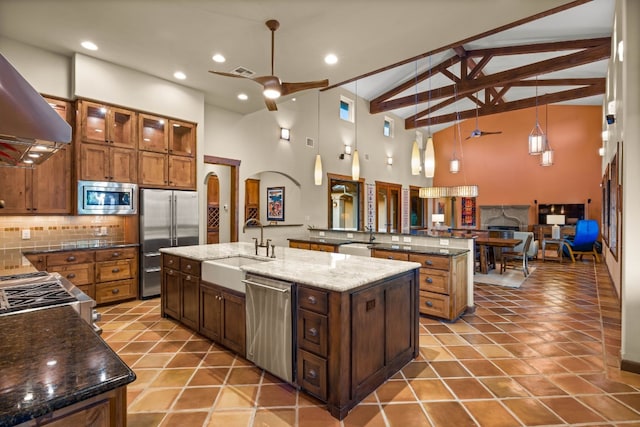 kitchen featuring beamed ceiling, decorative light fixtures, an island with sink, and stainless steel appliances